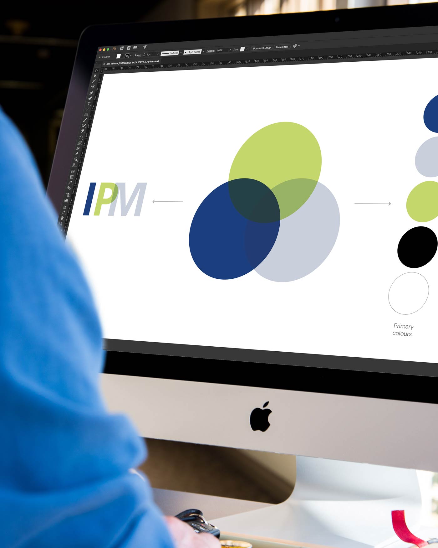 IPM brand redesign process displayed on an iMac screen, showcasing logo refinements and colour palette exploration.