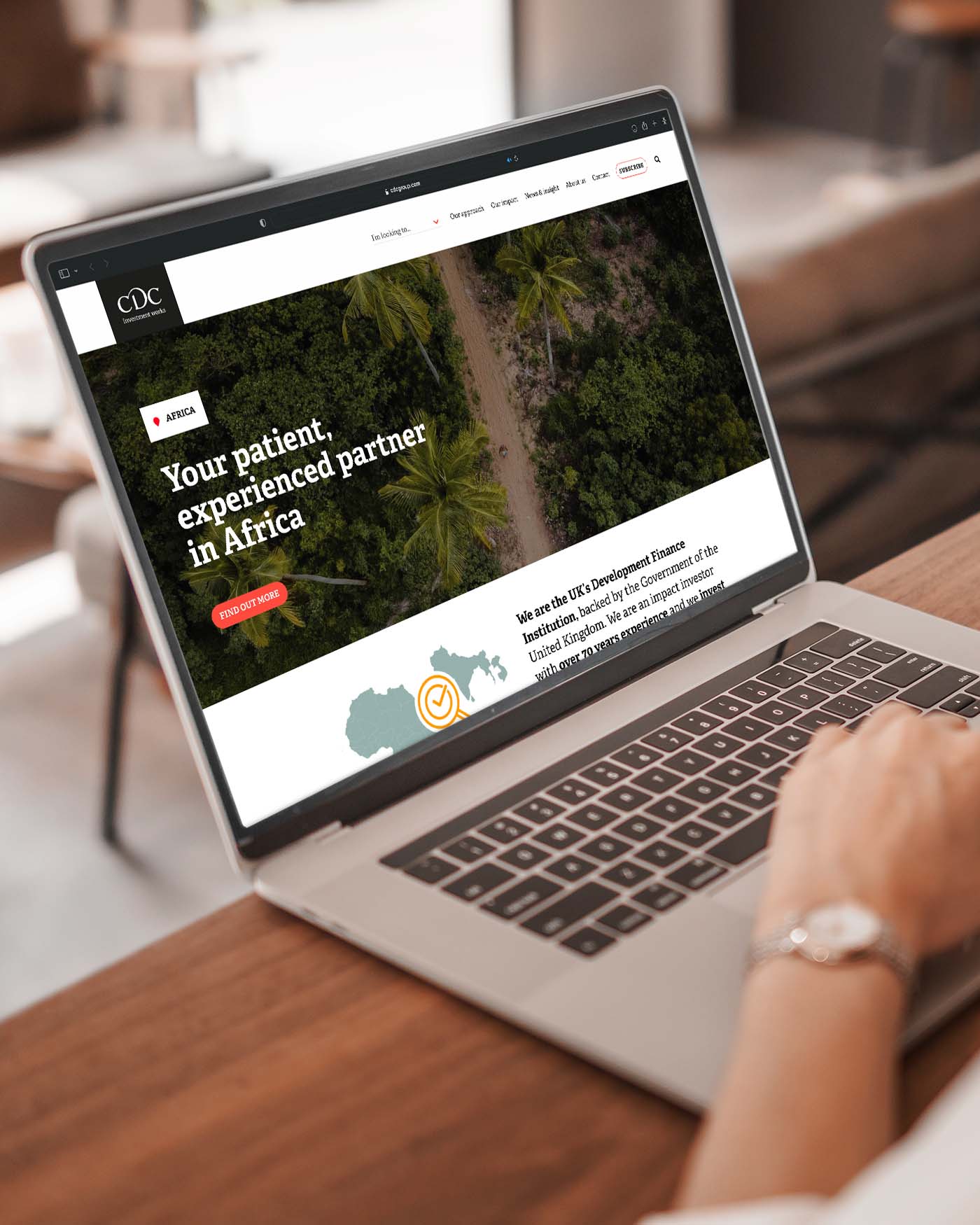 A person using a laptop displaying the CDC website, highlighting their role as a development finance institution and investment partner in Africa.